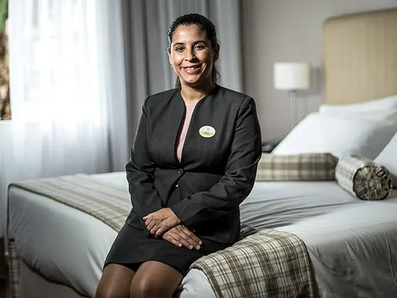 Governanta de terninho escuro sentada em um quarto arrumado, sorrindo